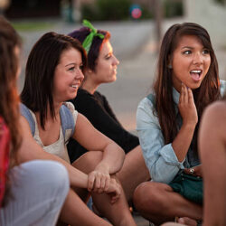 Shocked teenage girl sitting on the ground talking with friends